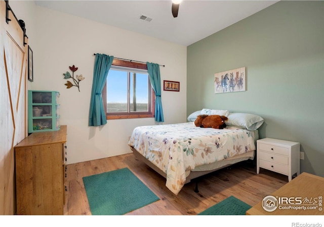 bedroom with a barn door, hardwood / wood-style flooring, and ceiling fan