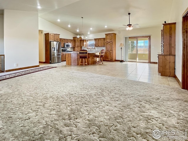 kitchen with ceiling fan, lofted ceiling, a kitchen bar, a kitchen island, and appliances with stainless steel finishes