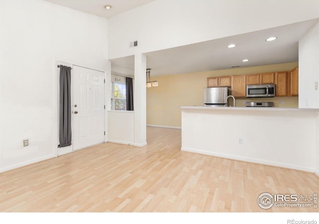 kitchen featuring a towering ceiling, appliances with stainless steel finishes, kitchen peninsula, and light hardwood / wood-style floors