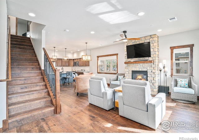 living room with a stone fireplace, dark hardwood / wood-style floors, and ceiling fan