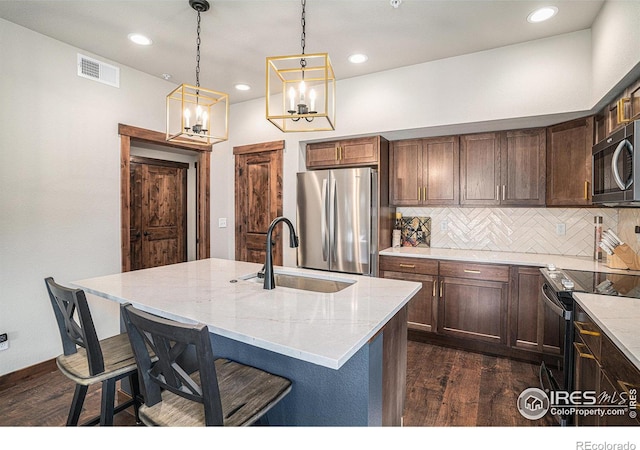 kitchen with stainless steel appliances, light stone countertops, sink, and a kitchen island with sink