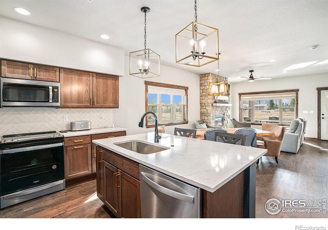 kitchen with a stone fireplace, stainless steel appliances, sink, and dark hardwood / wood-style flooring