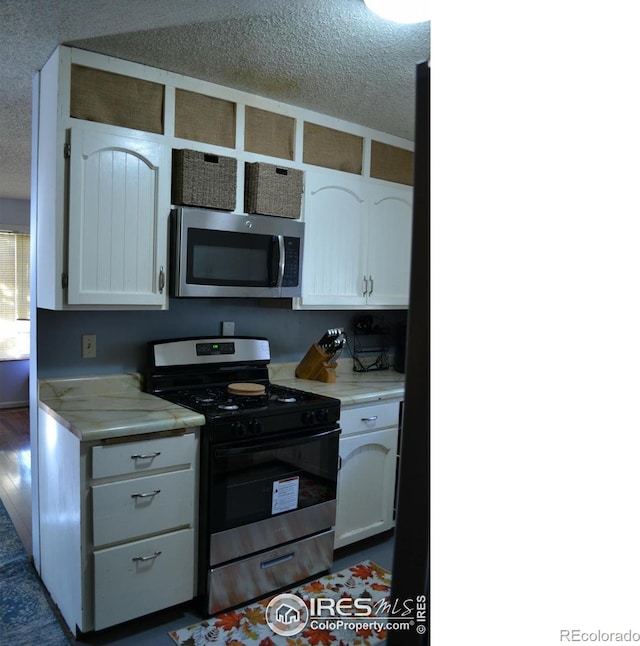 kitchen with a textured ceiling, white cabinets, and stainless steel appliances