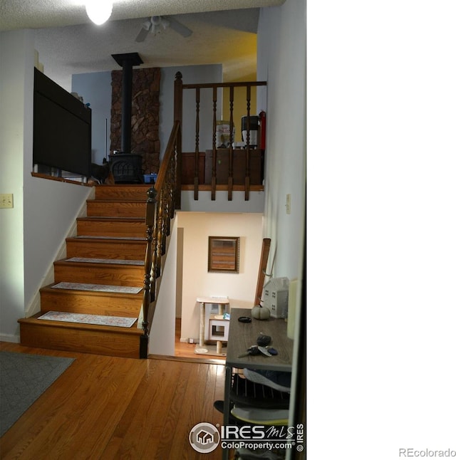 stairs with a wood stove, a textured ceiling, and hardwood / wood-style flooring