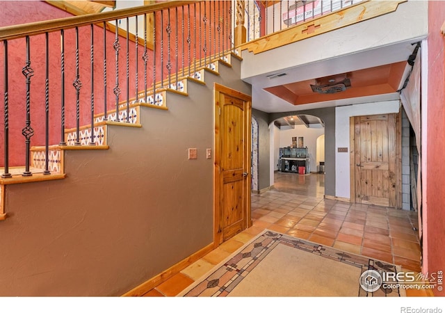 stairway with a tray ceiling and tile patterned flooring