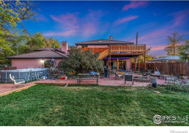 back house at dusk featuring a yard, a patio area, a pool side deck, and a fire pit