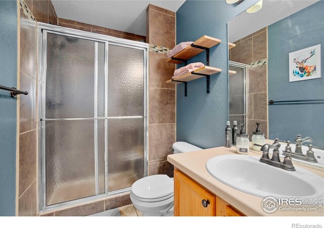 bathroom with a shower with door, vanity, and toilet