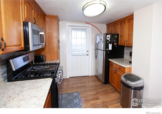 kitchen featuring appliances with stainless steel finishes, a textured ceiling, backsplash, and light hardwood / wood-style floors