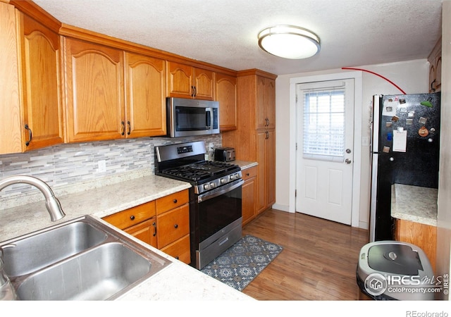 kitchen featuring decorative backsplash, hardwood / wood-style flooring, stainless steel appliances, sink, and a textured ceiling