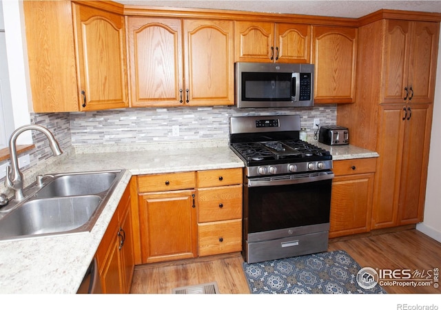 kitchen with appliances with stainless steel finishes, sink, light wood-type flooring, and decorative backsplash