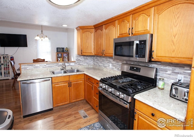 kitchen featuring sink, pendant lighting, a chandelier, appliances with stainless steel finishes, and light hardwood / wood-style floors