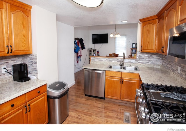 kitchen featuring decorative backsplash, sink, appliances with stainless steel finishes, a textured ceiling, and light hardwood / wood-style floors