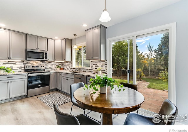 kitchen featuring hanging light fixtures, appliances with stainless steel finishes, light hardwood / wood-style flooring, gray cabinets, and sink