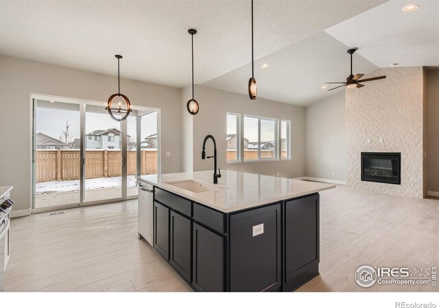 kitchen featuring lofted ceiling, stainless steel dishwasher, a large fireplace, a sink, and dark cabinets