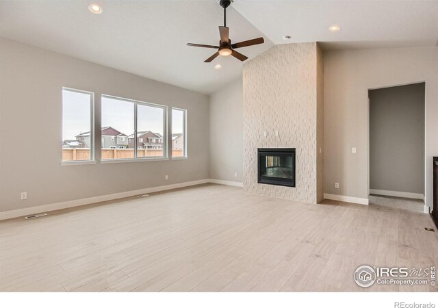 unfurnished living room with a glass covered fireplace, vaulted ceiling, ceiling fan, light wood-type flooring, and baseboards