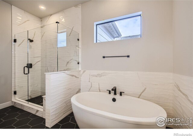 bathroom with a soaking tub, plenty of natural light, a marble finish shower, and tile walls