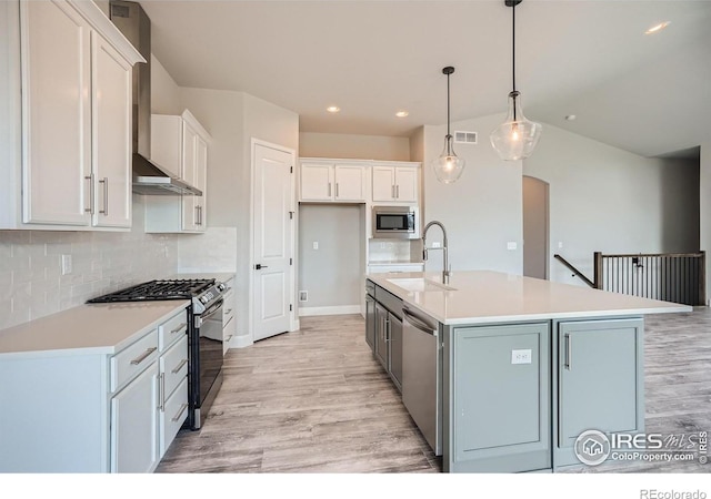 kitchen featuring appliances with stainless steel finishes, pendant lighting, sink, white cabinets, and a kitchen island with sink