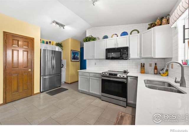 kitchen with sink, backsplash, stainless steel appliances, vaulted ceiling, and track lighting