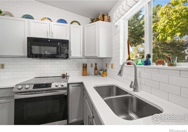 kitchen with lofted ceiling, backsplash, white cabinetry, stainless steel electric range oven, and sink