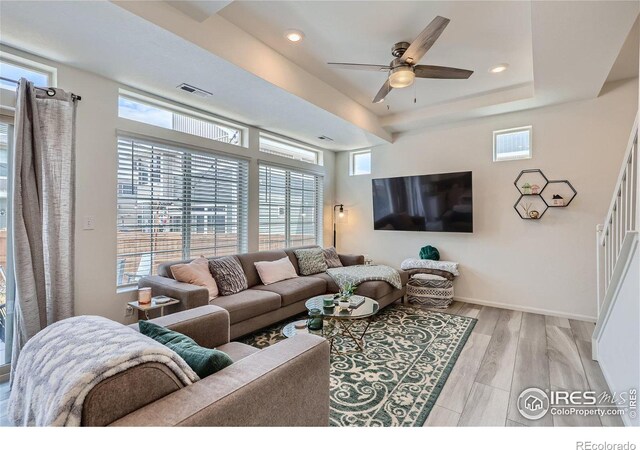 living room with light hardwood / wood-style flooring, a raised ceiling, and ceiling fan