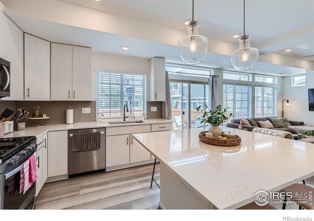 kitchen with sink, a kitchen island, backsplash, stainless steel appliances, and pendant lighting