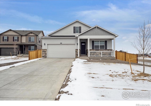 view of front of home featuring covered porch, a garage, fence, driveway, and stone siding