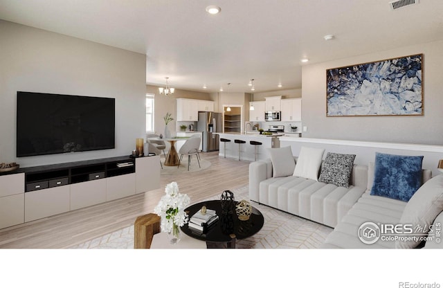 living room with light wood finished floors, recessed lighting, visible vents, and a notable chandelier