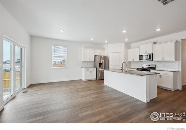 kitchen with decorative backsplash, appliances with stainless steel finishes, white cabinets, a sink, and wood finished floors