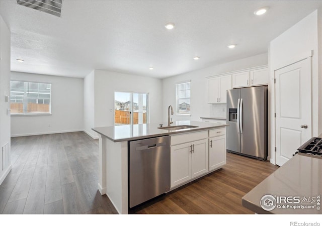 kitchen featuring dark wood finished floors, stainless steel appliances, visible vents, a sink, and an island with sink