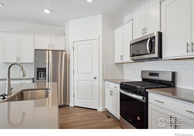 kitchen featuring dark wood-style floors, stainless steel appliances, backsplash, white cabinets, and a sink