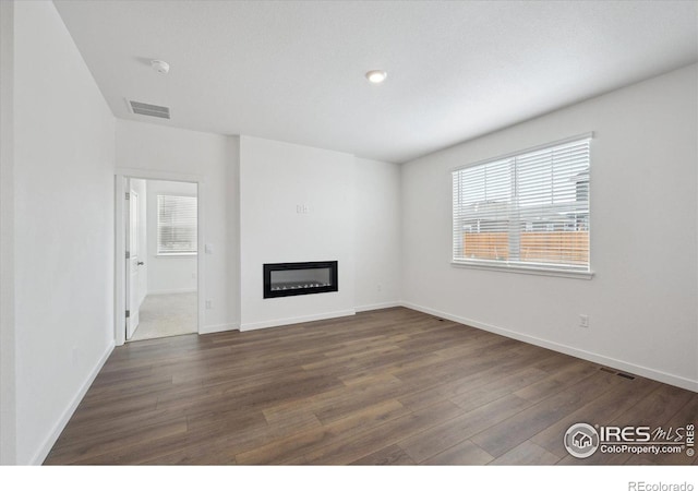 unfurnished living room featuring a glass covered fireplace, visible vents, dark wood finished floors, and baseboards