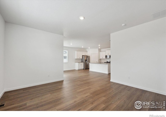 unfurnished living room with baseboards, visible vents, and dark wood-style flooring