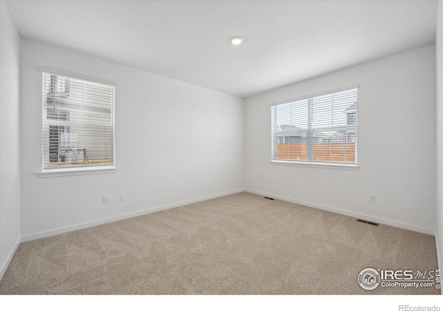 unfurnished room with carpet, visible vents, and baseboards