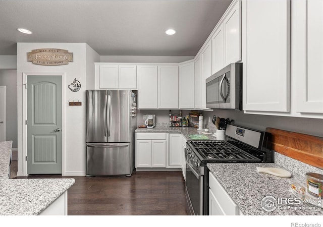 kitchen with white cabinetry, stainless steel appliances, light stone counters, and dark hardwood / wood-style flooring