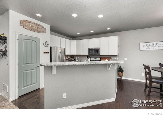 kitchen with a center island with sink, dark hardwood / wood-style flooring, a kitchen breakfast bar, white cabinetry, and stainless steel appliances