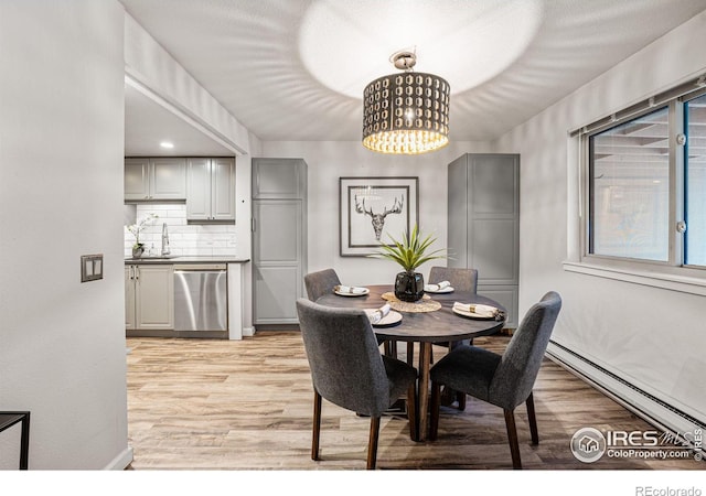 dining room featuring a baseboard radiator, light hardwood / wood-style flooring, a chandelier, and sink