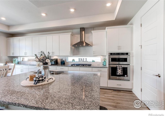 kitchen featuring white cabinetry, stainless steel appliances, and wall chimney range hood