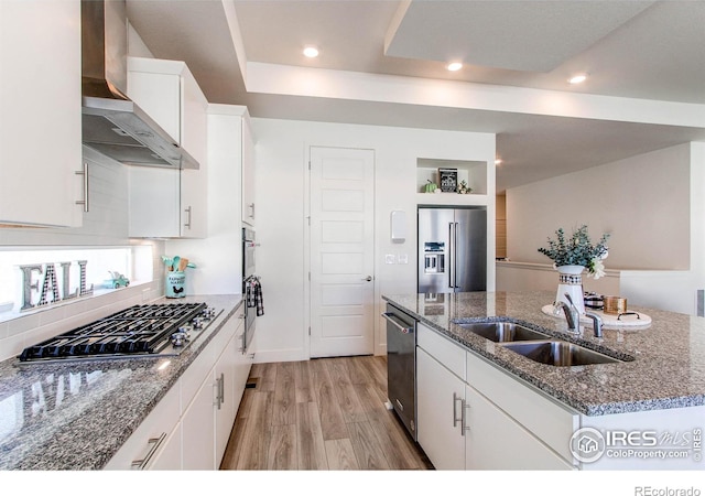 kitchen featuring wall chimney range hood, sink, white cabinets, appliances with stainless steel finishes, and light hardwood / wood-style floors