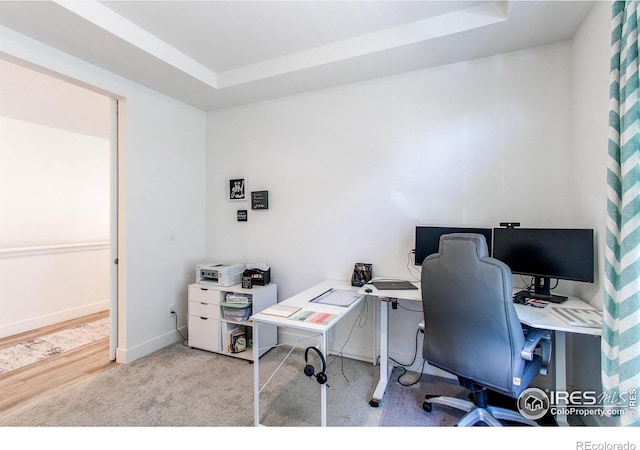 office with light hardwood / wood-style floors and a raised ceiling