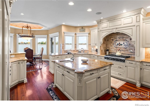 kitchen featuring sink, hanging light fixtures, decorative backsplash, dark hardwood / wood-style floors, and a kitchen island with sink