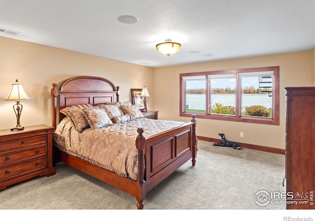 bedroom featuring a textured ceiling, a water view, and light colored carpet