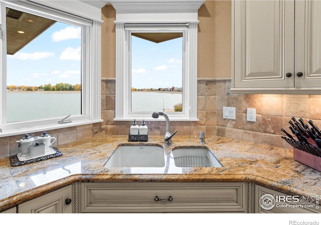 kitchen featuring light stone counters, sink, and a water view