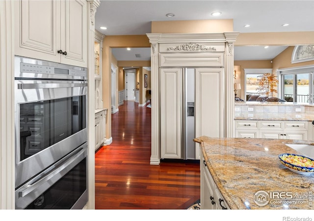 kitchen featuring tasteful backsplash, double oven, dark hardwood / wood-style flooring, paneled built in fridge, and light stone counters