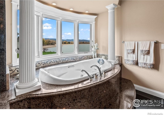 bathroom featuring a tub to relax in, a water view, and decorative columns