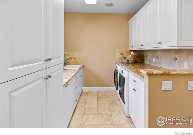 kitchen with light tile patterned floors, white cabinetry, washing machine and clothes dryer, sink, and light stone counters