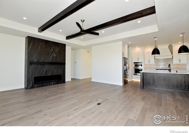 unfurnished living room with a raised ceiling, sink, light wood-type flooring, a premium fireplace, and beam ceiling