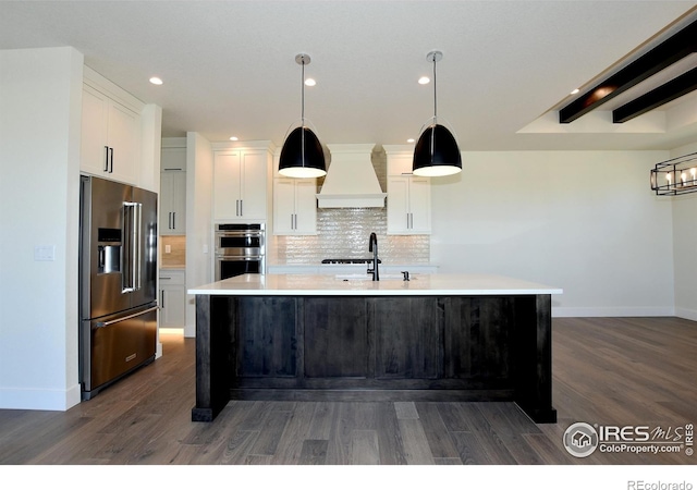 kitchen with white cabinetry, dark hardwood / wood-style floors, premium range hood, an island with sink, and appliances with stainless steel finishes