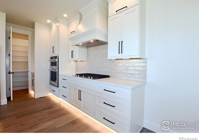 kitchen with stainless steel appliances, tasteful backsplash, light hardwood / wood-style floors, white cabinets, and custom range hood