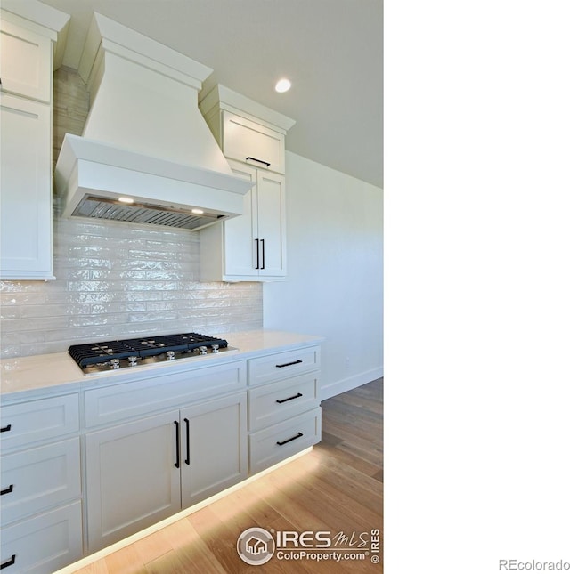 kitchen featuring stainless steel gas stovetop, decorative backsplash, white cabinets, custom exhaust hood, and light wood-type flooring