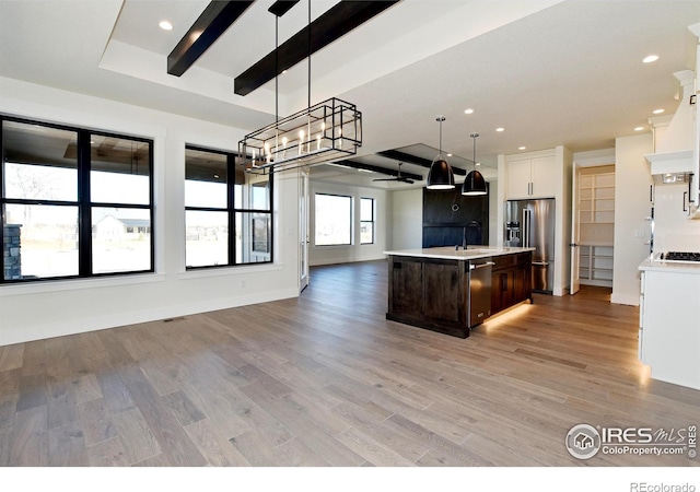 kitchen featuring appliances with stainless steel finishes, dark brown cabinets, decorative light fixtures, a center island with sink, and light hardwood / wood-style floors